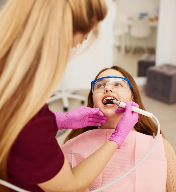 A dentist with pink latex gloves on is using a tool to clean a child's teeth.